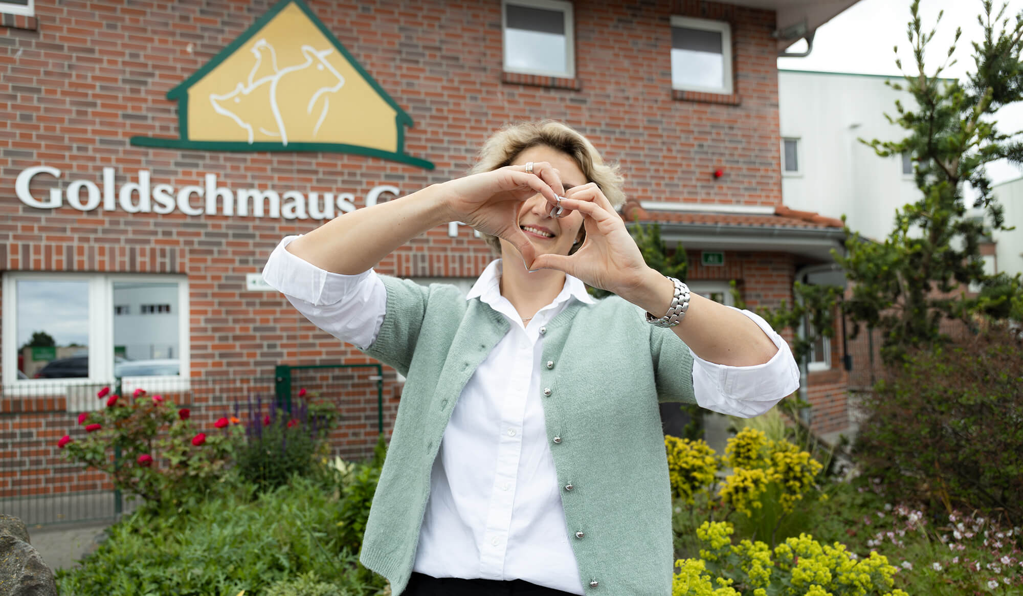Frau zeigt ein Herz vor dem Gebäude der Böseler Goldschmaus GmbH